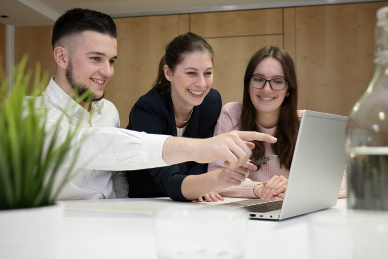 2 Auszubildende und 1 Ausbilderin arbeiten zusammen am Laptop